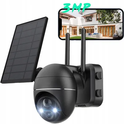 A black solar-powered security camera with two antennas, shown with a solar panel attached. A smartphone displaying a house is visible in the background.