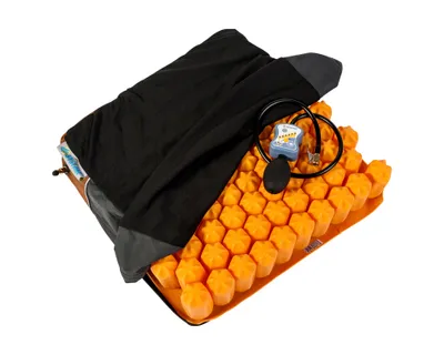 A close-up, angled studio shot of an orange, honeycomb-shaped air cushion with a black cover and a small air pump.