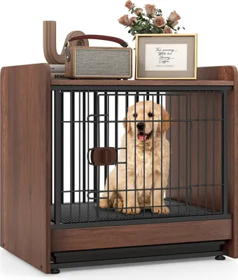A golden retriever dog sits inside a wooden dog crate that is designed to look like a nightstand. The crate has a black metal cage door and a brown wooden frame. On top of the crate, there is a vintage-style radio, a framed picture with text, and a small v