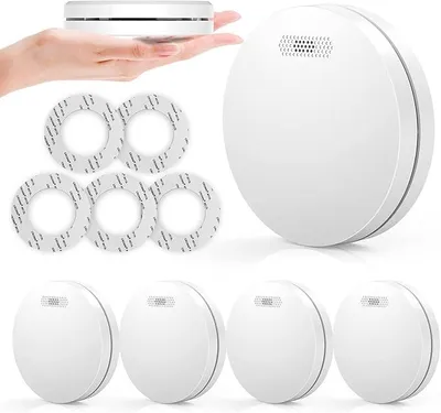 A hand holding a smoke detector with other smoke detectors and adhesive tapes arranged around it.