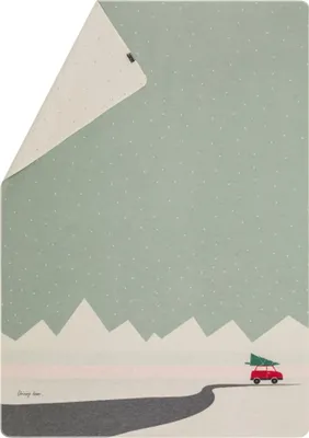 A blanket with a winter scene illustration of mountains, a road, and a red car carrying a Christmas tree.