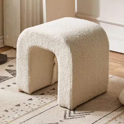 A fluffy, U-shaped stool sits on a patterned rug in a room.