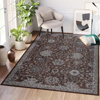 A living room scene with a rug, chair, plants, and artwork.