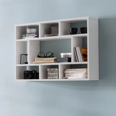 A white modular wall shelf mounted on a light blue wall, filled with various decorative items and books.