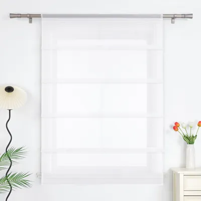 A white sheer Roman blind hangs on a window, with a floor lamp and a vase of tulips on the right.