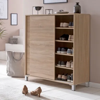 A shoe cabinet in a hallway with shoes on display and a large tote bag next to it.