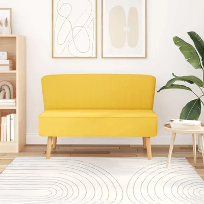 A yellow sofa is placed in a room with a bookshelf and artwork on the wall.