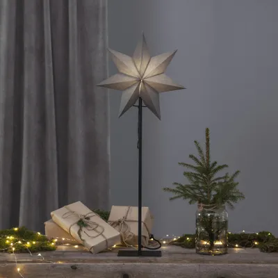A star-shaped lamp is displayed on a wooden surface with gifts and a small Christmas tree, suggesting a festive or decorative setting.