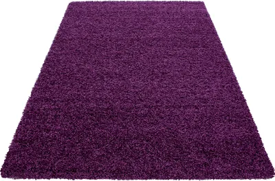 A close-up, angled view of a shaggy, violet rug on a white background.
