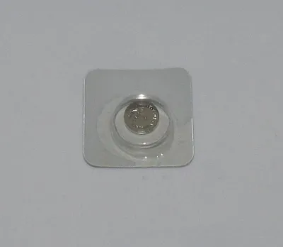 A single button cell battery in a clear plastic blister pack, lying on a light gray surface.