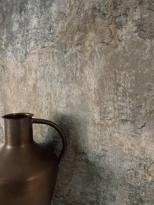A close-up shot of a vintage-style bronze jug against a textured, weathered wall.