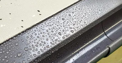 A close-up view of a gray gutter system with many water droplets on its surface.