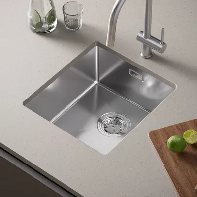 A stainless steel kitchen sink installed in a countertop, with a faucet and some limes on a cutting board nearby.