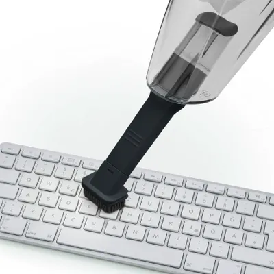 A mini vacuum cleaner with a brush attachment is being used to clean a computer keyboard.