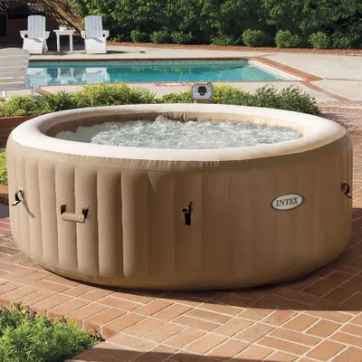 An inflatable hot tub is set up on a brick patio next to a swimming pool.
