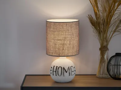A table lamp with a white ceramic base and a gray fabric shade sits on a wooden table.