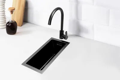 A black sink and faucet on a white countertop with a tiled backsplash.