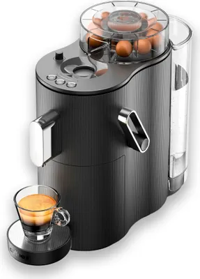 A black coffee machine with a clear top compartment holding coffee capsules, a glass cup of espresso, and a water reservoir.
