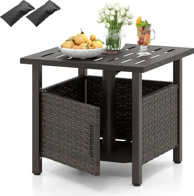 An outdoor side table with a woven basket base and a slatted top, set against a white background. It is decorated with a bowl of fruit, a vase of flowers, and a drink.