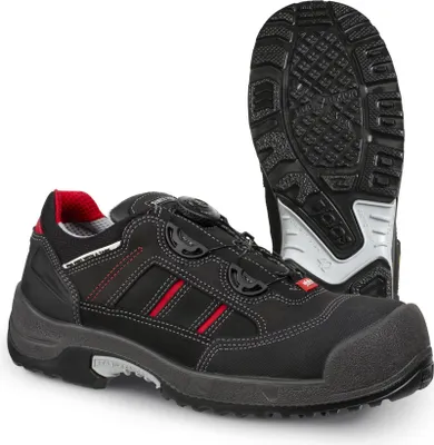 A black safety shoe with red accents and a white sole is shown against a white background. Another shoe is visible in the background, showing its sole.