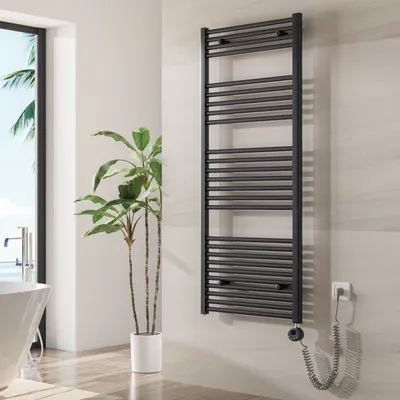 A modern bathroom with a white bathtub, a potted plant, and a black electric towel warmer mounted on a tiled wall.