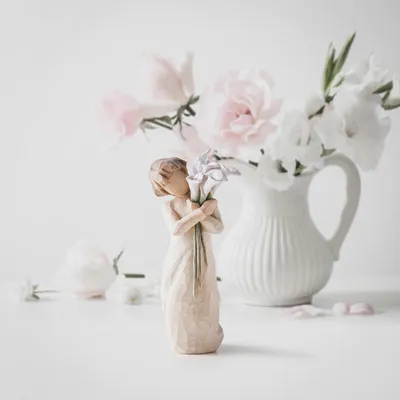 A figurine of a girl holding flowers stands in front of a vase of flowers.