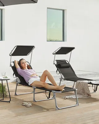 A woman relaxing on a black sun lounger with a canopy, with another sun lounger in the background.