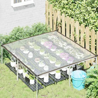 A clear plastic tarp greenhouse setup in a garden with potted plants.