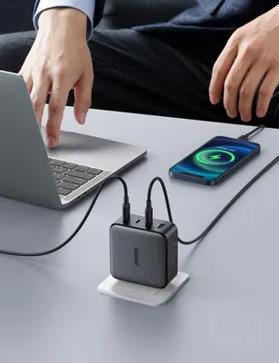 A person's hands are shown using a laptop while a phone and a multi-port charger are plugged in and charging on a desk.