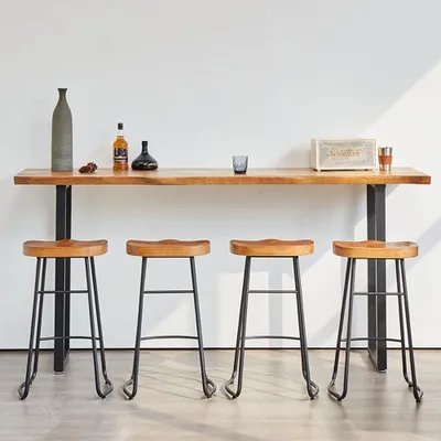 A set of four bar stools in front of a wooden bar counter against a white wall.