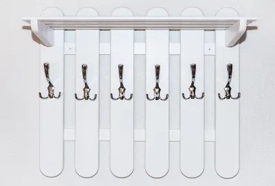 A white coat rack with multiple hooks mounted on a textured wall.