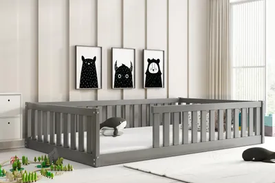 A child's bed with a grey wooden frame and a white mattress, decorated with black and white monster-themed artwork on the wall and whale-shaped plush toys on the bed and floor.