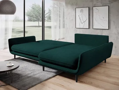 A modern living room with a green sectional sofa that has been converted into a bed, placed in front of a large window with sheer curtains.