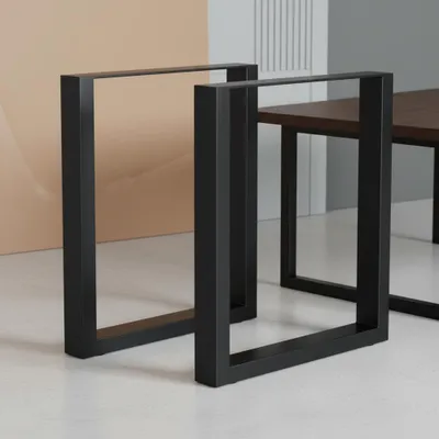 Two black metal table legs are shown in a studio setting with a beige and gray background.