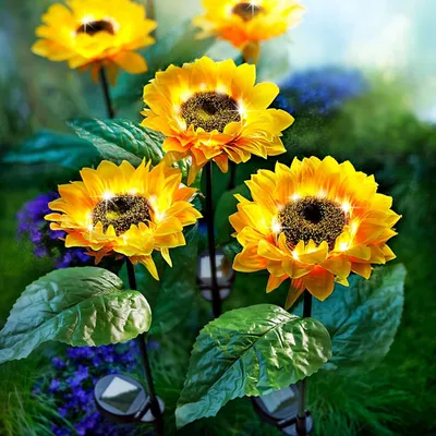 Solar-powered garden stakes shaped like sunflowers are illuminated at dusk in a garden setting.