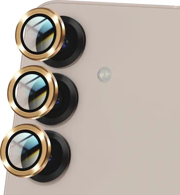 Close-up of three gold-rimmed camera lens protectors on the back of a light-colored smartphone.