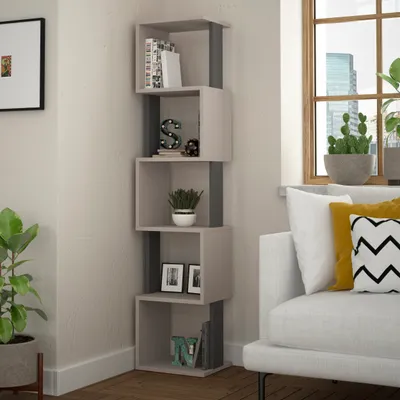 A corner bookshelf filled with books and decorative items, next to a window with plants and a sofa.