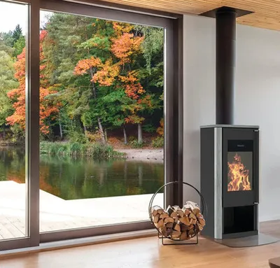 A modern living room with a fireplace and a view of autumn trees and a lake through a large window.
