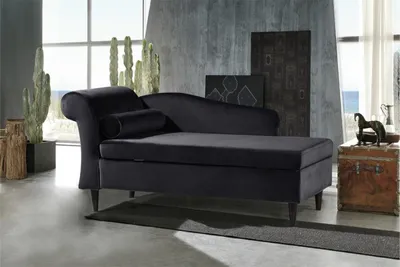 A black chaise lounge is placed in a modern living room setting with large windows and decorative plants.