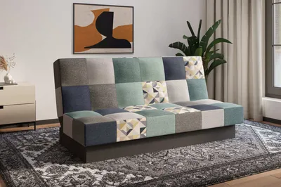 A patchwork sofa is shown in a living room setting, placed on a rug in front of a piece of abstract art and a plant.