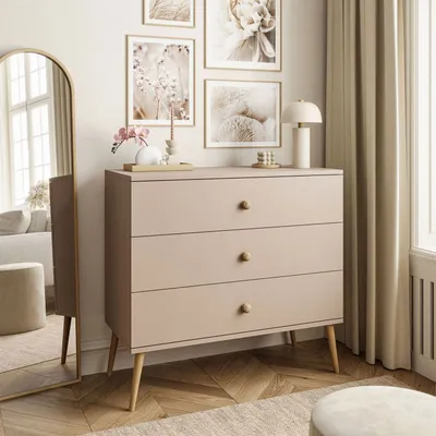 A dresser with three drawers is placed in a room with artwork on the wall and a large mirror.