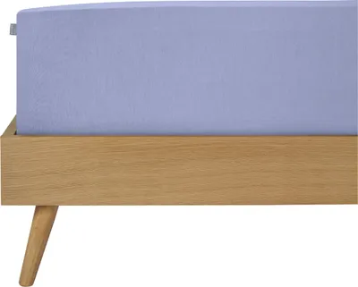 A close-up side view of a bed with a lavender fitted sheet on a wooden bed frame.