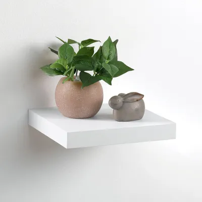 A white floating shelf with a potted plant and a small bunny figurine.