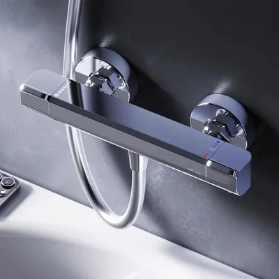 A close-up shot of a modern chrome shower thermostat mounted on a gray tiled wall, with a white bathtub edge visible in the foreground.
