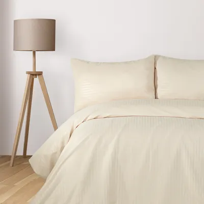 A bed with beige bedding and pillows, next to a floor lamp.