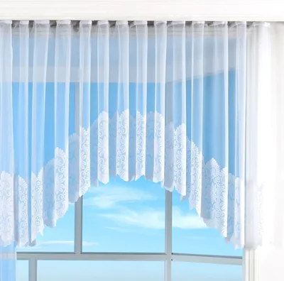 A white lace curtain with a floral pattern hangs in front of a window, revealing a blue sky with clouds.