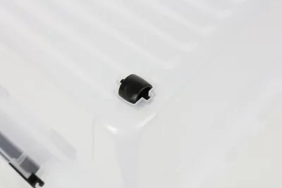 A close-up view of a black plastic clip attached to the corner of a transparent storage box.