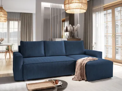A modern living room with a blue sectional sofa and an ottoman, decorated with dried flowers and a woven pendant light.