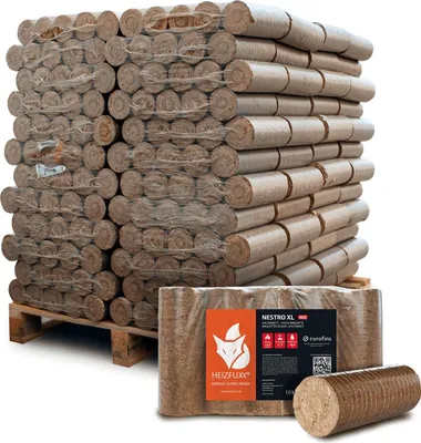 A large stack of compressed wood briquettes on a pallet, with a smaller package and a single briquette in the foreground.
