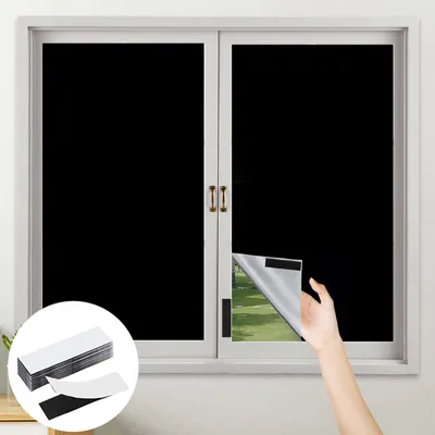 A hand is shown peeling back a black window film from a window, revealing a green outdoor scene. A stack of adhesive strips is in the foreground.